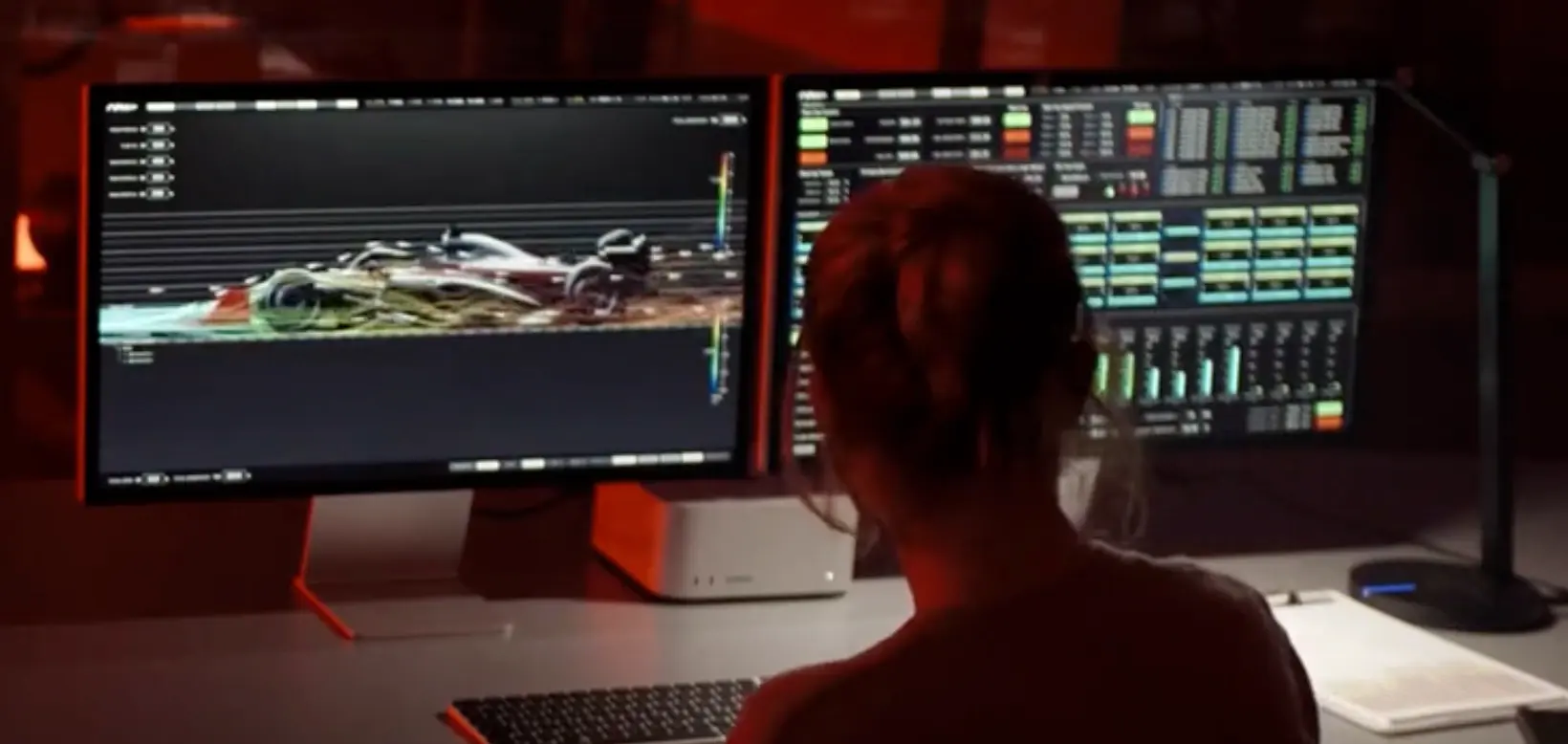 Still from F1 (2025): an engineer at a desk with two monitors, the left showing the car in side view with airflow and a vertical colour scale, the right a dense grid of teal and yellow readout tiles and bar charts