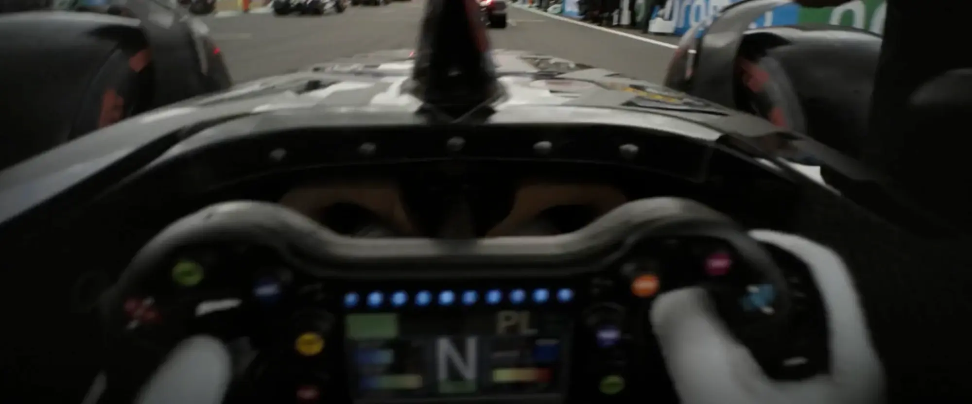Still from F1 (2025): the driver's view from the cockpit on the grid, the track and cars ahead above the nose, the steering wheel below with a row of blue shift lights and its screen showing N