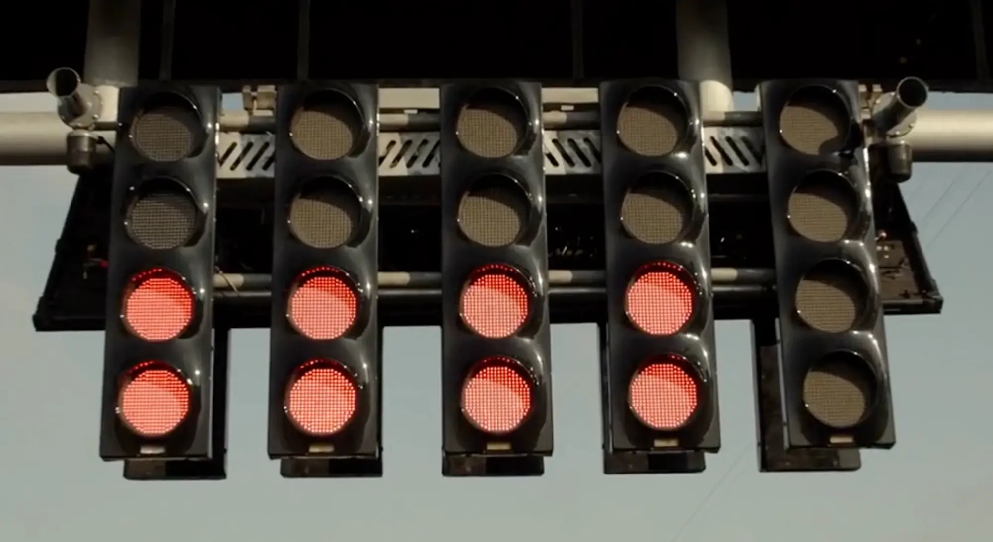 Still from F1 (2025): the start gantry's five columns of lights against the sky, the lower two lights lit red on four columns and the fifth column still dark